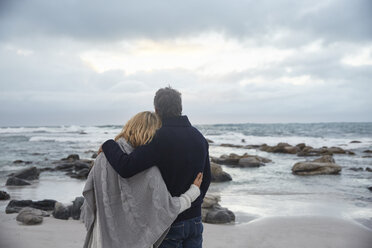 Serene affectionate couple hugging on winter beach looking at ocean - HOXF02605