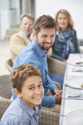 Porträt eines lächelnden Jungen, der mit seiner Familie auf der Terrasse zu Mittag isst - HOXF02625
