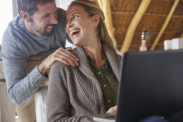 Happy couple laughing and using laptop - HOXF02628