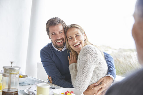 Glückliches, zärtliches Paar, das sich beim Frühstück im Innenhof umarmt und lacht - HOXF02632