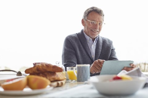 Älterer Mann benutzt digitales Tablet beim Frühstück im Innenhof, lizenzfreies Stockfoto