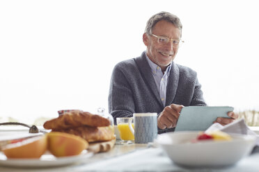 Älterer Mann benutzt digitales Tablet beim Frühstück im Innenhof - HOXF02659