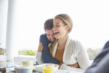 Zärtliches Paar, das sich beim Frühstück auf der Terrasse umarmt und lacht - HOXF02661