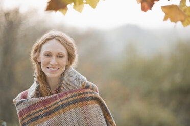 Portrait smiling woman wrapped in blanket in autumn park - HOXF02691