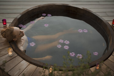 Gelassene Frau, die im Whirlpool mit Blumen und Kerzen auf der Terrasse badet - HOXF02695