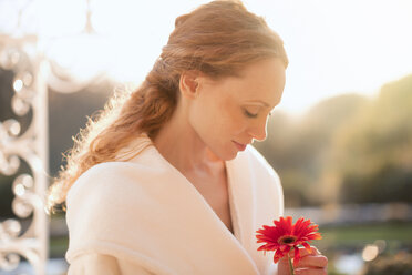 Gelassene Frau hält rote Gerbera-Gänseblümchen auf einer sonnigen Veranda - HOXF02702