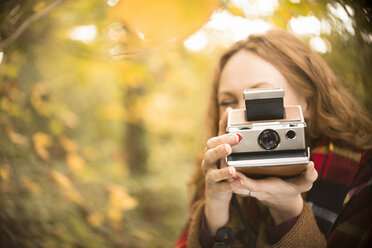 Portrait woman using old-fashioned instant camera in autumn woods - HOXF02705