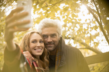 Lächelndes Paar nimmt Selfie mit Kamera-Handy unter Herbstbaum - HOXF02707