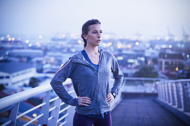 Determined female runner resting on urban footbridge at dawn - HOXF02717