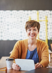 Portrait smiling businesswoman using digital tablet drinking coffee at cafe table - HOXF02734