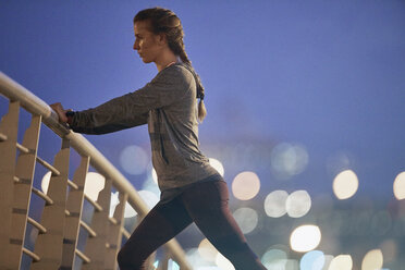 Entschlossene Läuferin streckt ihre Beine auf einer Fußgängerbrücke in der Morgendämmerung - HOXF02735