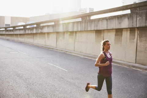Weibliche Läuferin läuft auf einer sonnigen städtischen Straße, lizenzfreies Stockfoto