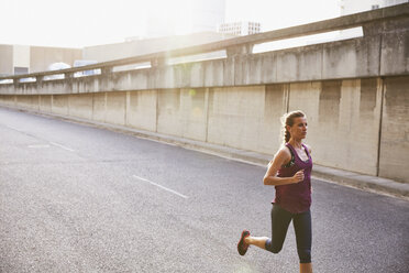 Weibliche Läuferin läuft auf einer sonnigen städtischen Straße - HOXF02748