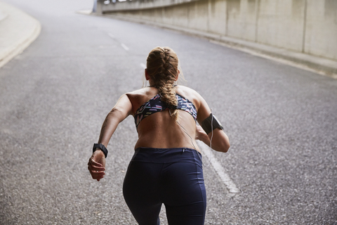 Fitte Läuferin mit mp3-Player-Armband beim Laufen auf einer städtischen Straße, lizenzfreies Stockfoto