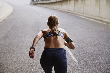 Fitte Läuferin mit mp3-Player-Armband beim Laufen auf einer städtischen Straße - HOXF02760