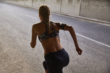 Fitte Läuferin in Sport-BH und mp3-Player-Armband beim Laufen auf einer städtischen Straße - HOXF02764