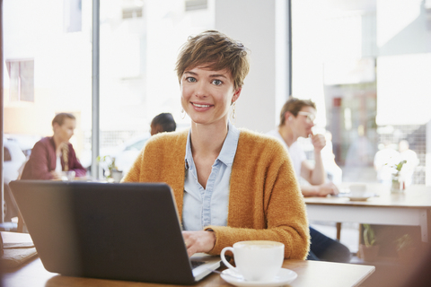 Porträt einer lächelnden Geschäftsfrau, die in einem Café Kaffee trinkt und am Laptop arbeitet, lizenzfreies Stockfoto