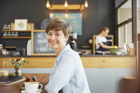 Porträt einer lächelnden Frau, die am Kaffeetisch Kaffee trinkt - HOXF02781