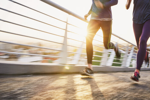 Runner couple running on sunny urban footbridge at sunrise - HOXF02782