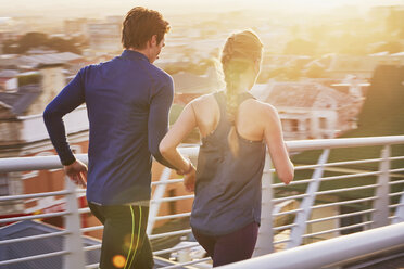 Runner couple running on sunny urban footbridge at sunrise - HOXF02784