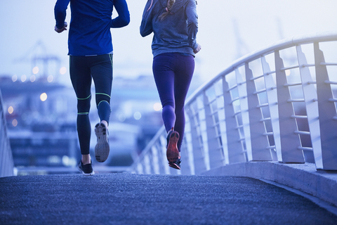 Läuferpaar beim Laufen auf einer Fußgängerbrücke in der Morgendämmerung, lizenzfreies Stockfoto