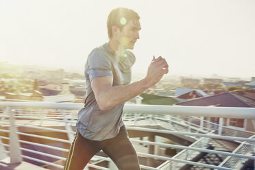 Determined male runner running on sunny urban footbridge at sunrise - HOXF02786