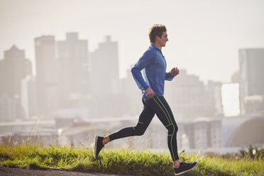 Male runner running on sunny urban street - HOXF02792