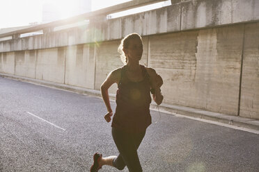 Silhouette einer Läuferin, die auf einer sonnigen städtischen Straße läuft - HOXF02802