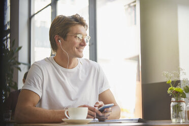 Lächelnder Mann mit Kopfhörern und mp3-Player hört Musik und trinkt Kaffee in einem Cafe - HOXF02806