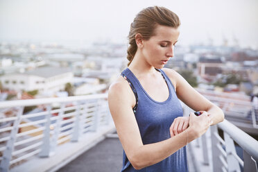 Läuferin prüft Smartwatch-Fitness-Tracker auf einer Fußgängerbrücke in der Stadt - HOXF02809