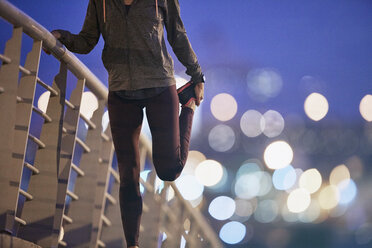 Läuferin streckt Bein auf Fußgängerbrücke in der Abenddämmerung - HOXF02814