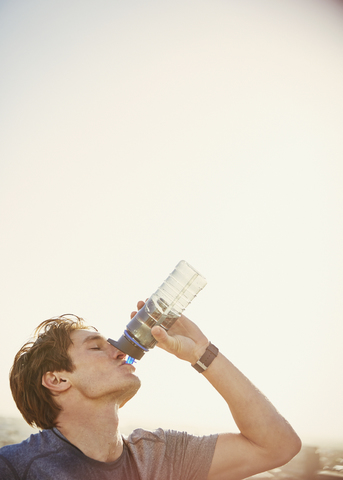 Durstiger männlicher Läufer, der Wasser aus einer Wasserflasche trinkt, lizenzfreies Stockfoto