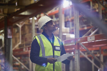Arbeiter mit Klemmbrett schaut auf Regale in einem Vertriebslager - HOXF02835