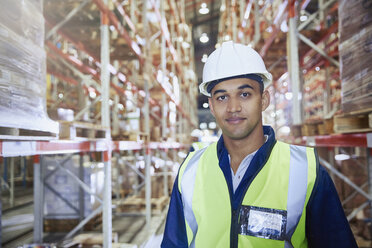 Portrait confident worker in hard-hat in distribution warehouse aisle - HOXF02837