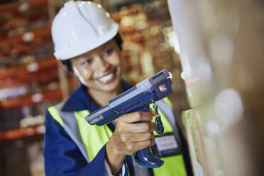 Smiling female worker using scanner scanning cardboard box in distribution warehouse - HOXF02840