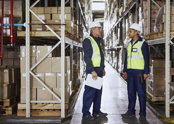 Manager and worker talking in aisle of distribution warehouse - HOXF02868