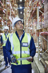 Worker with clipboard and scanner looking up in distribution warehouse - HOXF02874