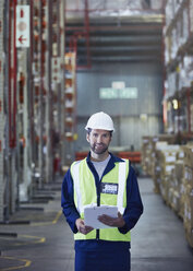 Portrait smiling worker with clipboard in distribution warehouse - HOXF02876