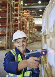 Portrait smiling worker using scanner scanning boxes in distribution warehouse - HOXF02884