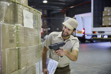 Truck driver worker scanning pallet of cardboard boxes at distribution warehouse loading dock - HOXF02902