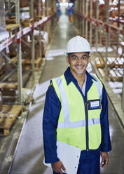 Portrait smiling worker with clipboard in distribution warehouse aisle - HOXF02904