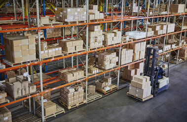 Worker operating forklift moving cardboard boxes along distribution warehouse shelves - HOXF02907