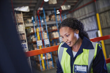 Lächelnde Arbeiterin, die in einem Vertriebslager nach unten schaut - HOXF02908