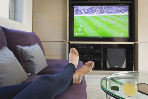 Persönliche Perspektive Frau mit nackten Füßen oben beobachten Fußballspiel im Fernsehen im Wohnzimmer - HOXF02915