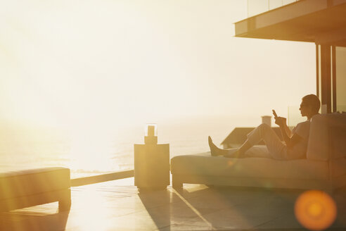 Silhouette Frau mit Handy auf Chaise Lounge auf Luxus-Balkon mit Sonnenuntergang Blick auf das Meer - HOXF02916