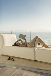 Woman using digital tablet relaxing laying on chaise lounge on luxury balcony with ocean view - HOXF02936