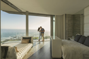 Affectionate couple hugging on modern luxury home showcase bedroom balcony with ocean view - HOXF02937