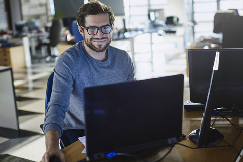 Porträt eines lächelnden Geschäftsmannes, der am Computer im Büro arbeitet, lizenzfreies Stockfoto