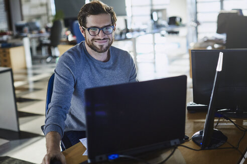 Porträt eines lächelnden Geschäftsmannes, der am Computer im Büro arbeitet - HOXF02961