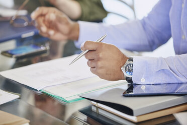 Businessman holding pen over paperwork in meeting - HOXF02964